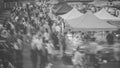 Black and white photograph of a busy outdoor market scene with many people walking past large canopy tents.